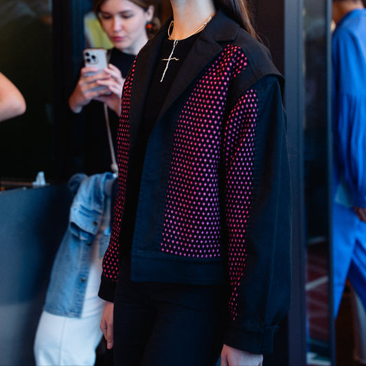 Woman wearing a black jacket with red and pink pattern, standing in a reflective surface setting.