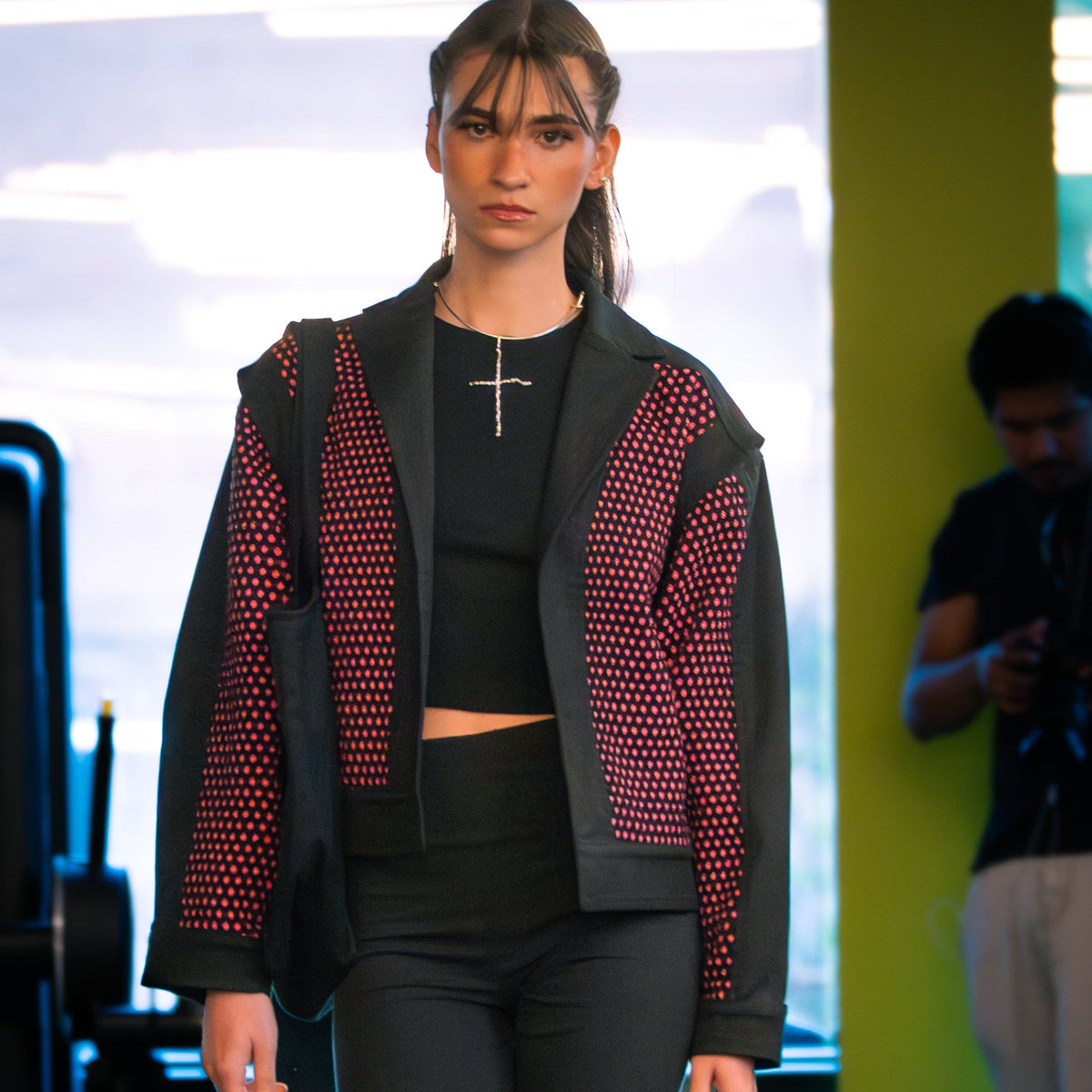 Model walking on a fashion show runway wearing a black and pink handwoven jacket.